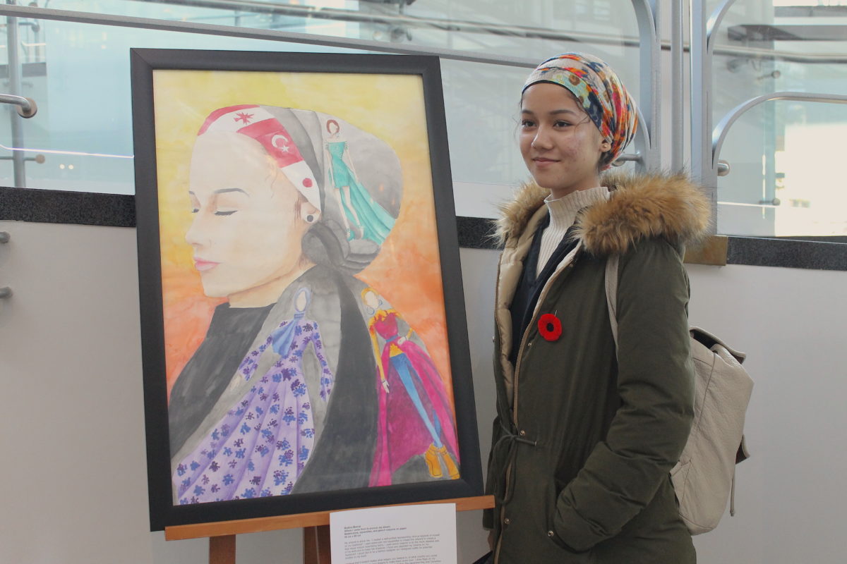 A student stands with their artwork for the My Name Is Asher Lev Lobby Display